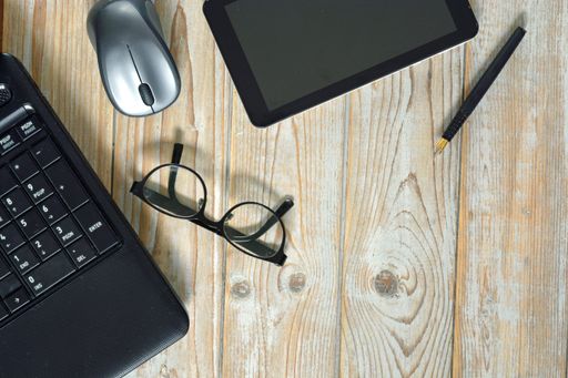 An overhead shot of a laptop, digital tablet with a wireless mouse and optical eyeglasses isolated on a wooden surface - work at home concept