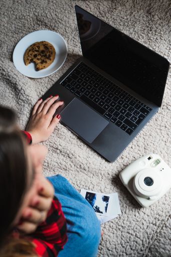 A vertical shot of a female sitting on a blanket with her laptop, coffee and a cookie