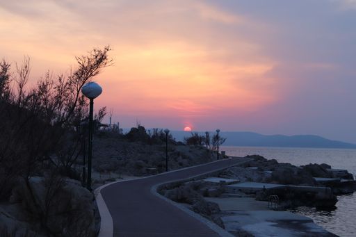 A scenic view of a road along the ocean during a vibrant sunset in the cloudy sky