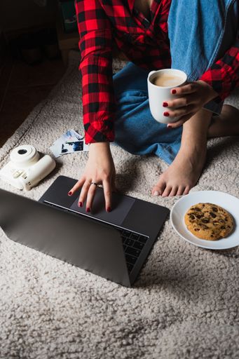 A vertical shot of a female sitting on a blanket with her laptop and coffee