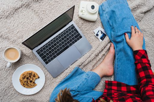 A horizontal shot of a female sitting on a blanket with her laptop, coffee and a cookie