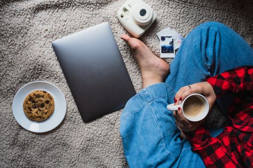 A horizontal shot of a female sitting on a blanket with her laptop and coffee