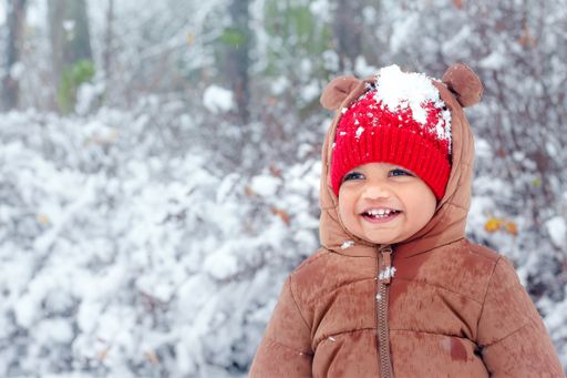 Happy child in bear outfit enjoying snow at winter park.