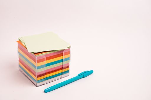 A closeup shot of a box with colorful papers and a blue pen isolated on a light-colored background