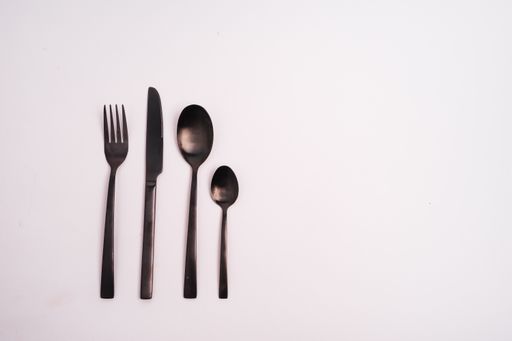 A closeup shot of a knife, fork, and two spoons isolated on a light-colored background