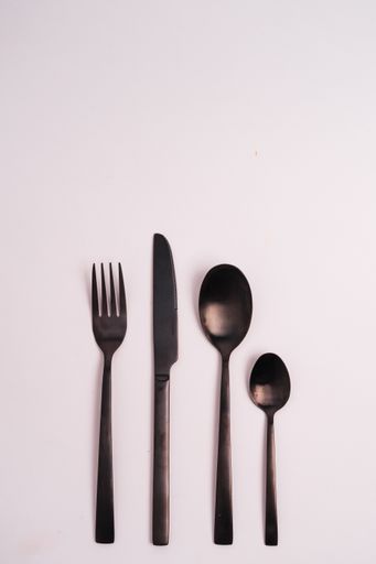 A vertical shot of two spoons, a knife, and a fork isolated on a light-colored background