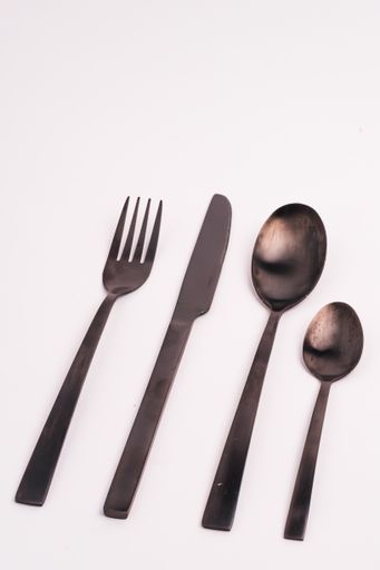A vertical closeup shot of a knife, fork, and two spoons isolated on a light-colored background