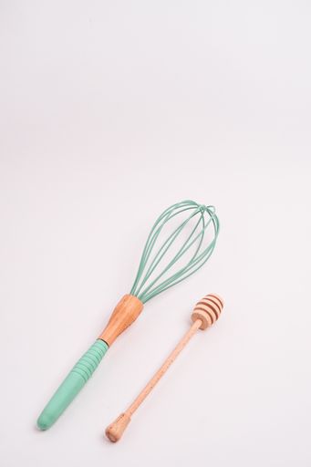 A vertical closeup shot of a whisk and a honey dipper isolated on a light-colored background
