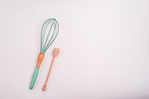 A closeup shot of a whisk and a honey dipper isolated on a light-colored background