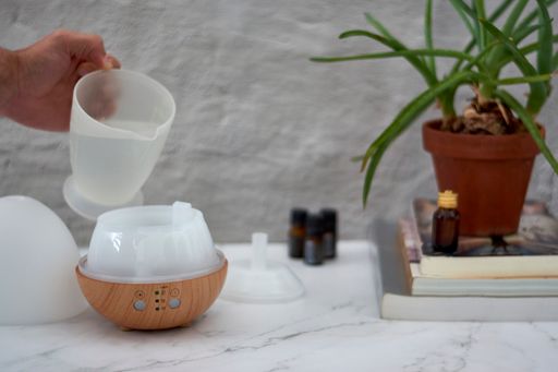 A closeup of a hand setting a humidifier on a marble table near books with aloe vera plant and essential oils