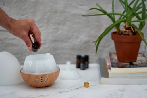 A closeup of a hand setting a humidifier on a marble table near books with aloe vera plant and essential oils