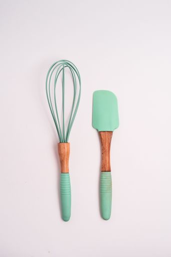 A vertical closeup shot of green kitchen whisk and shovel isolated on a light-colored background