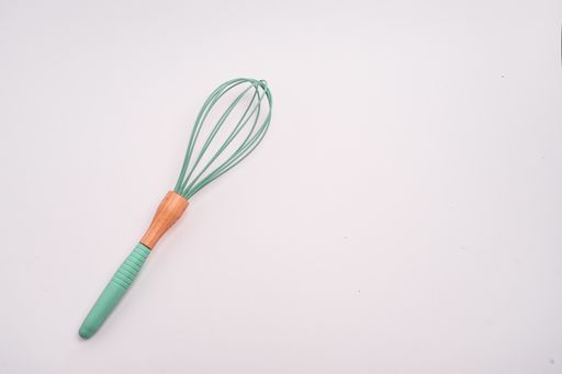 A closeup shot of a green whisk isolated on a light-colored background