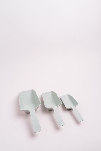 A vertical closeup shot of three white plastic kitchen scoops isolated on a light-colored background