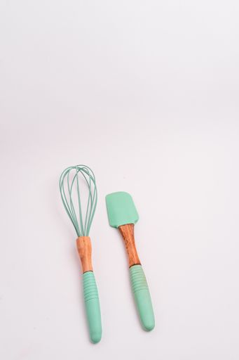 A vertical closeup shot of green kitchen whisk and shovel isolated on a light-colored background