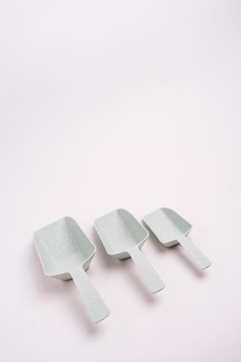 A vertical closeup shot of three white plastic kitchen scoops isolated on a light-colored background