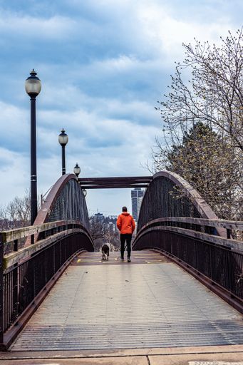 A vertical shot of a man walking on a rusty old iron walkway bridge on the train tracks