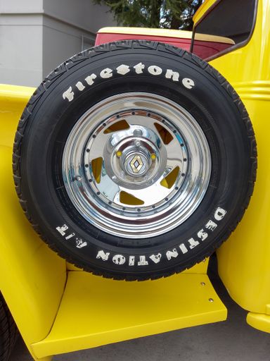 Firestone logo and brand on rubber tire. Spare wheel at the side of the bed of an old pickup truck. Traditional fileteado ornaments. Classic car show.