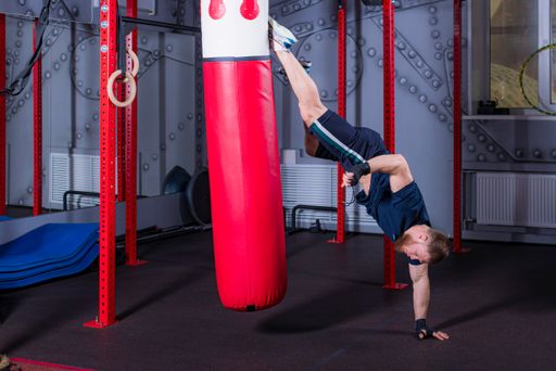 Young MMA fighter in inverted state delivers strong straight kick on red boxing pear to area of alleged head of opponent. Training process in gym.