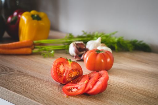 A closeup shot of tomatoes, garlic, baby carrots, bell peppers and mortar and pestle on top of a wooden surface