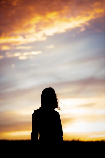 A vertical shot of the girl's silhouette standing in the field against the sunset.