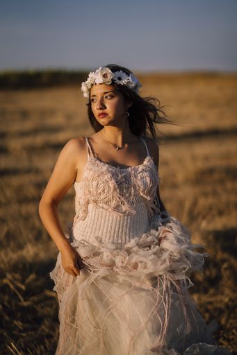 A vertical shot of a young caucasian female in white dress and white flower wreath posing in a field