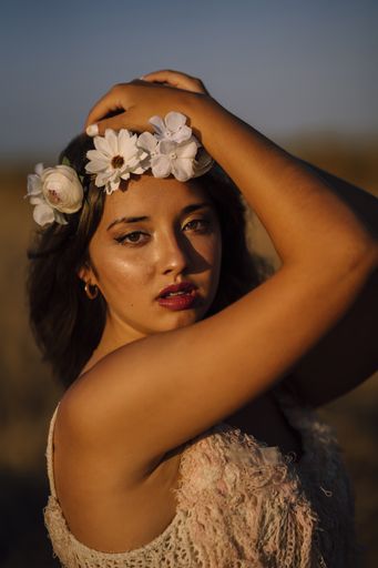 A vertical shot of a young caucasian female in white dress and white flower wreath posing in a field