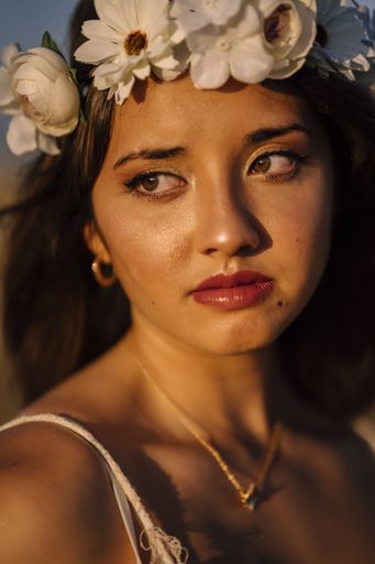 A vertical shallow focus shot of a young caucasian female in white dress and white flower wreath posing in a field