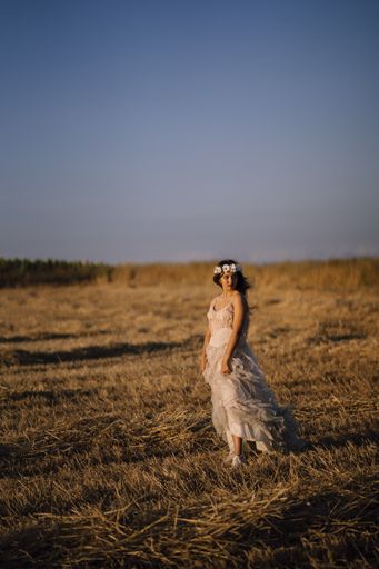 A vertical shot of a young caucasian female in white dress and white flower wreath posing in a field