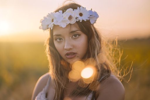 A horizontal shallow focus shot of a young caucasian female with a flower wreath posing in a field