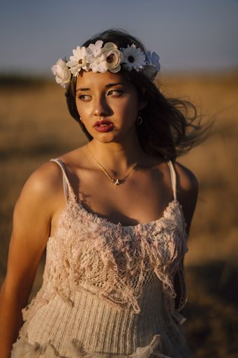 A vertical shot of a young caucasian female in white dress and white flower wreath posing in a field
