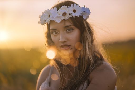 A horizontal shallow focus shot of a young caucasian female with a flower wreath posing in a field