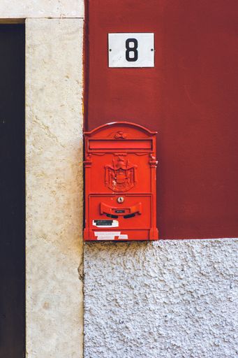A vertical closeup shot of a red mailbox with the city crest engraved on it and a house plaque above