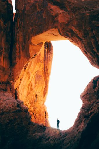 A vertical shot of a person standing under a rocky arch in the Grand Canyon, Arizona