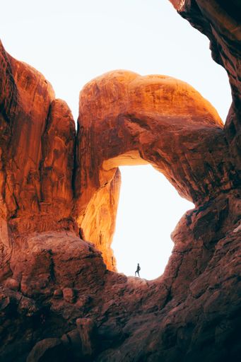 A vertical shot of a person standing under a rocky arch in the Grand Canyon, Arizona