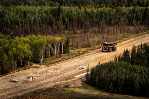 A giant oilsands mining truck driving through a road surrounded by tall green trees