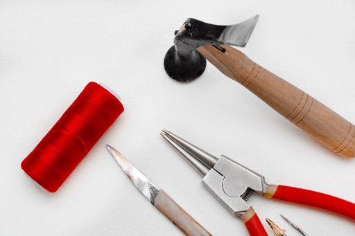 A closeup of the tools isolated on white background. The hammer, circlip pliers, knife, red thread.