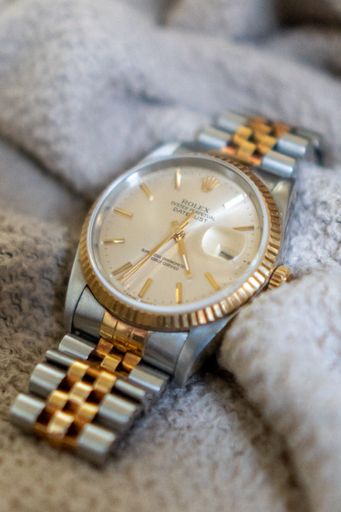 A vertical closeup of a Rolex Datejust two-tone watch on a soft fabric