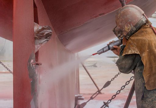 worker, sandblasting the corroded hull of a sailing vessel with a high pressure sandblasting syst
