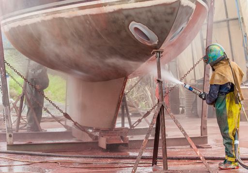 worker, sandblasting the corroded hull of a sailing vessel with a high pressure sandblasting syst