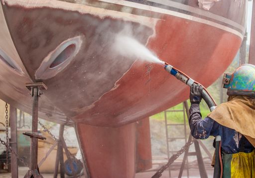 worker, sandblasting the corroded hull of a sailing vessel with a high pressure sandblasting syst