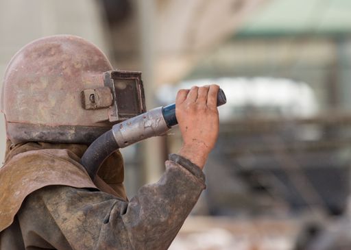 worker, sandblasting the corroded hull of a sailing vessel with a high pressure sandblasting syst