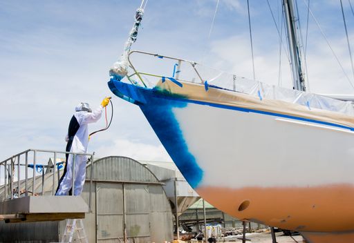 Spray painter with full body protection and mask painting the hull of sailboat