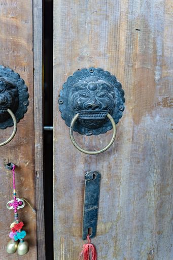 An old wooden door with a metal door handle in form of a lion's head with ring and a suspended Chinese accessory