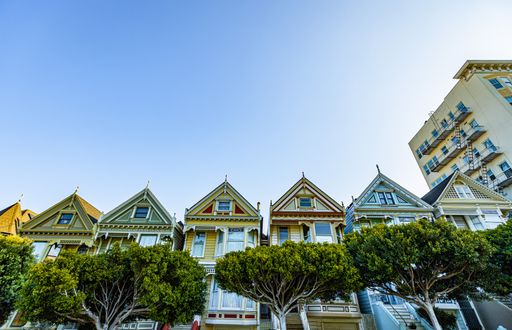 A low angle of colorful Victorian houses and green trees against blue sky in San Francisco, USA