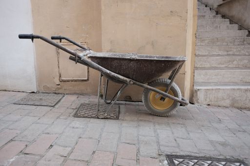 An old wheelbarrow with a weathered wall and stairs in the background
