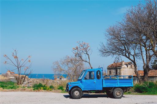 A blue old truck with some trees at the background