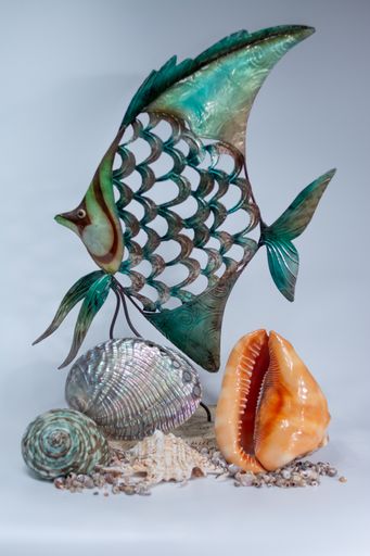 A vertical shot of a fish figurine with different seashells under it on a white surface and background