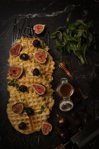 A top view of figs and blackberries on the Belgian waffles with honey on a black table