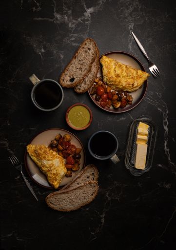 A top view of the omelets with mushrooms and vegetables and slices of bread on a black table